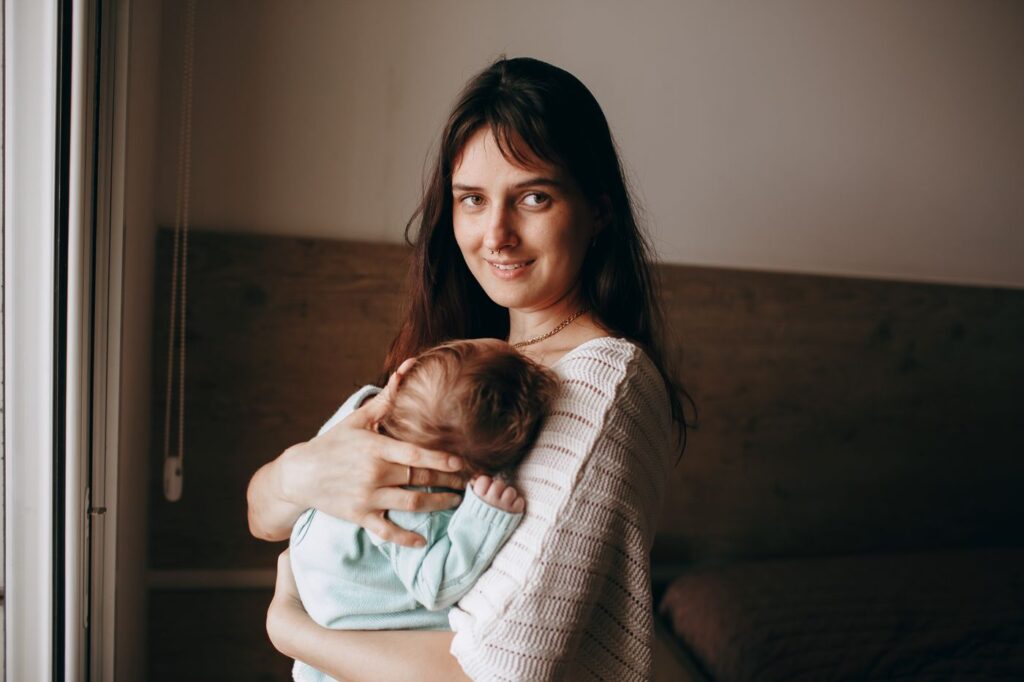 Madre junto a la ventana con su bebé dormido en brazos