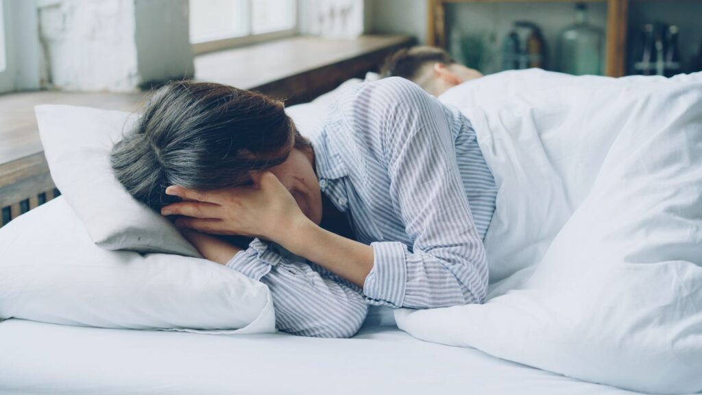 Mujer en la cama con gesto de preocupación, luz suave
