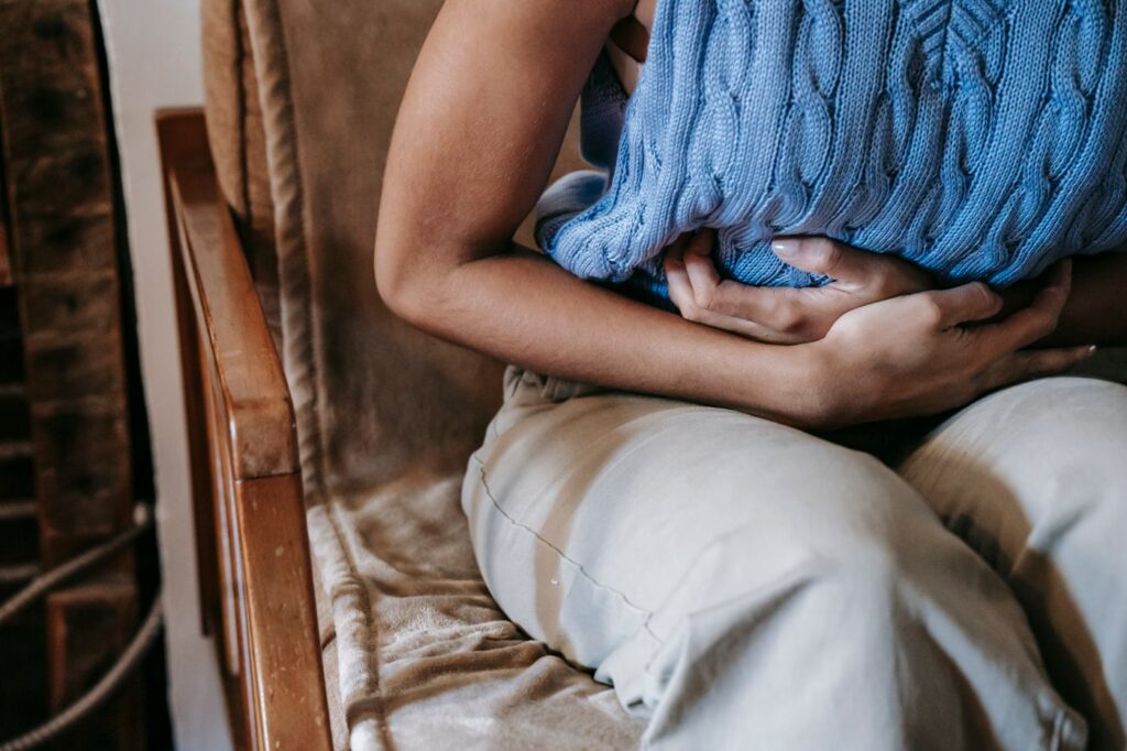 Mujer sentada en el sofá con las manos sobre el vientre por dolor