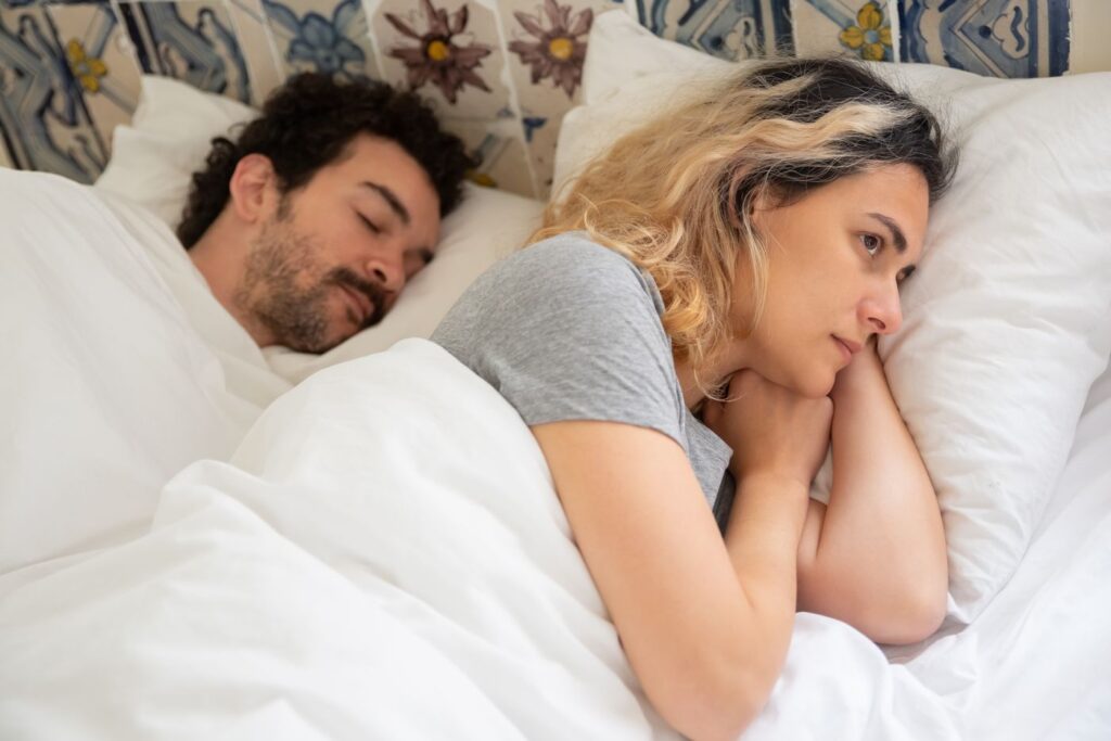 Mujer despierta y pensativa en la cama junto a su pareja dormida
