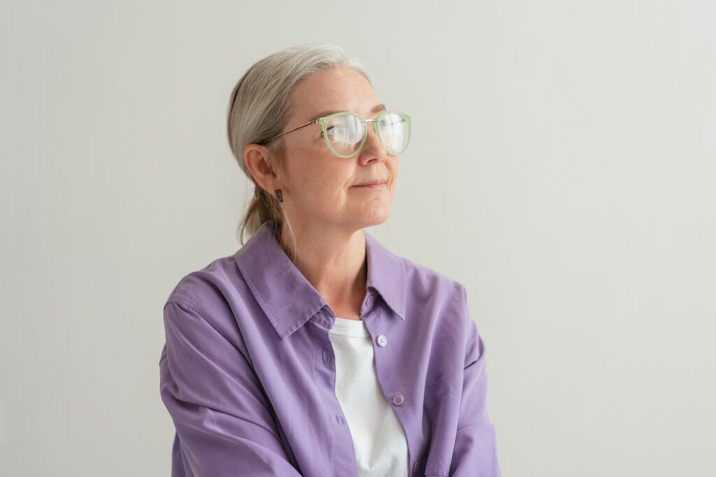 Mujer de pelo canoso con gafas y camisa morada, pensativa